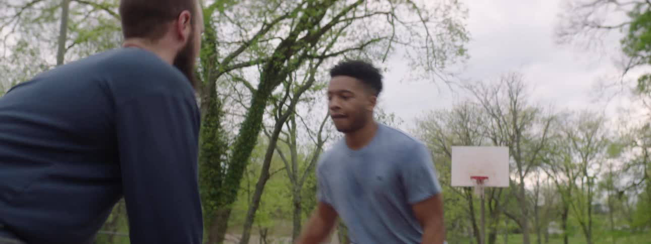 Close-up slow motion shot of two young men playing a friendly game of one-on-one basketball at a local park