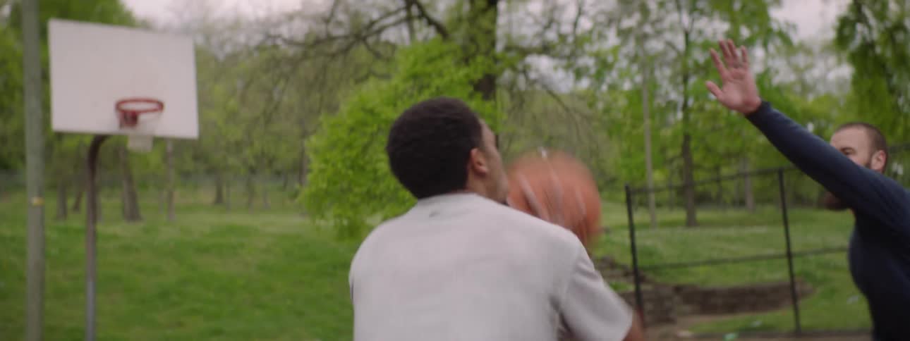 A group of diverse friends pass and shoot the ball while playing a game of pickup basketball on an outdoor court in slow motion