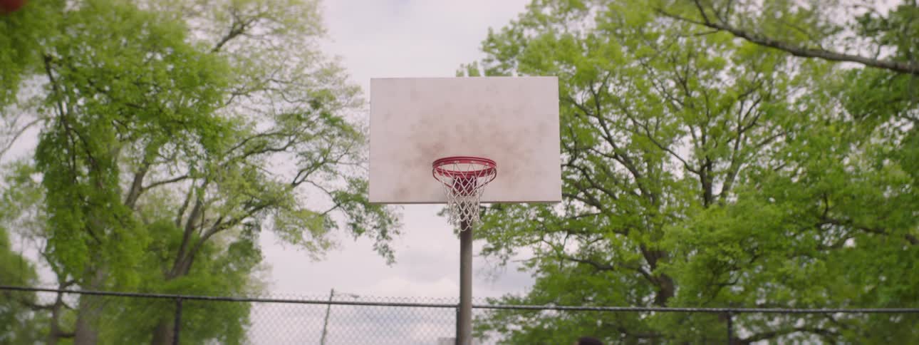 Slow motion close-up of a basketball repeatedly swishing through the net on an outdoor court surrounded by trees