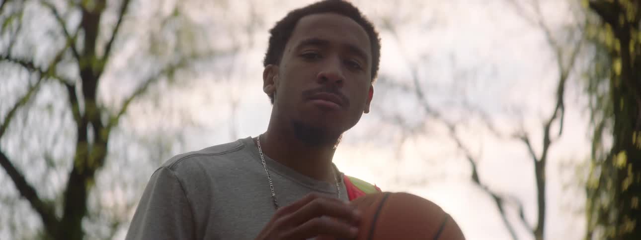 Cinematic close-up of a focused young man holding a basketball outdoors with a powerful sun flare