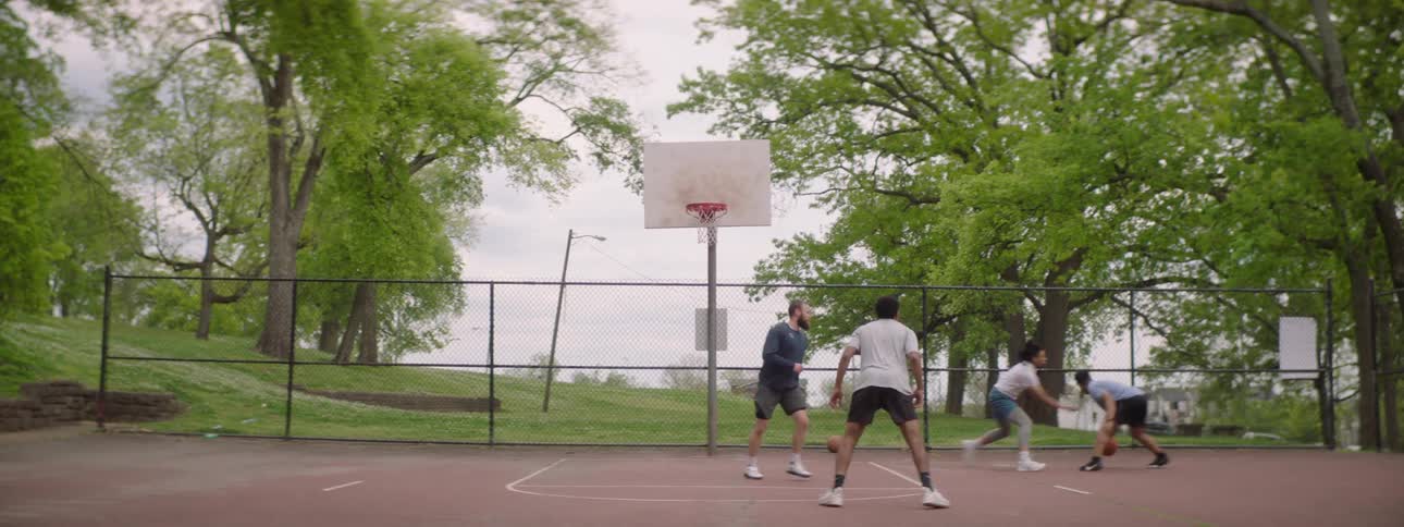 Slow motion footage shows a group of diverse friends playing a friendly game of basketball on an outdoor court in a park