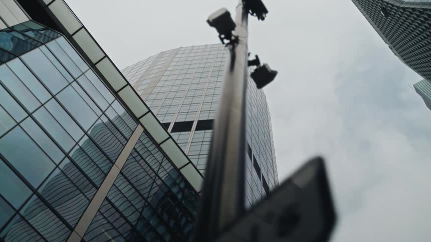 A slow, low-angle reveal shot of towering glass skyscrapers in a modern city against a cloudy sky