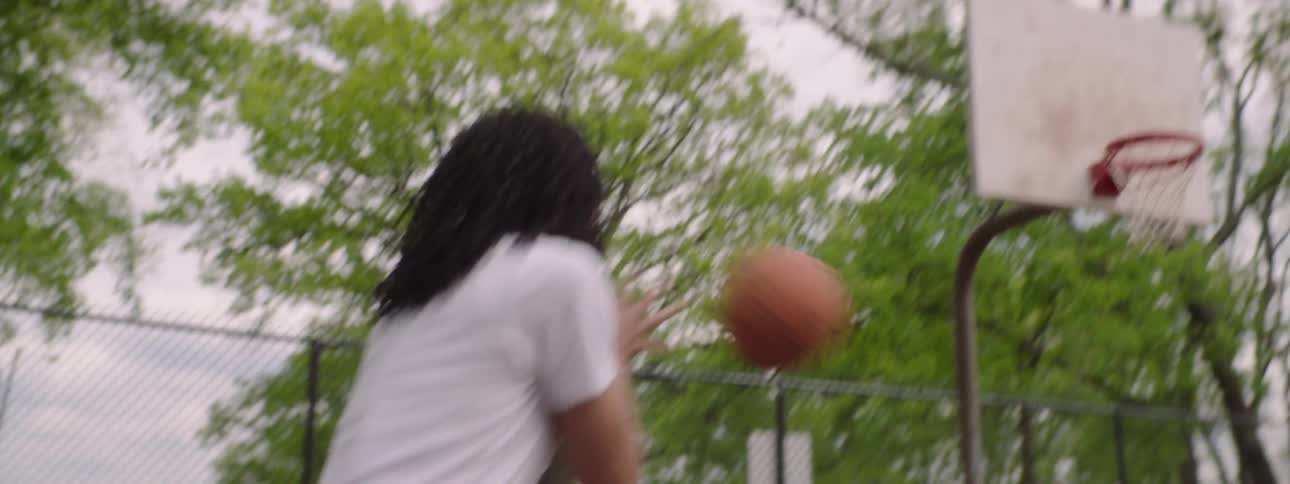 Slow motion over the shoulder shot of a basketball player making a perfect shot on an outdoor court