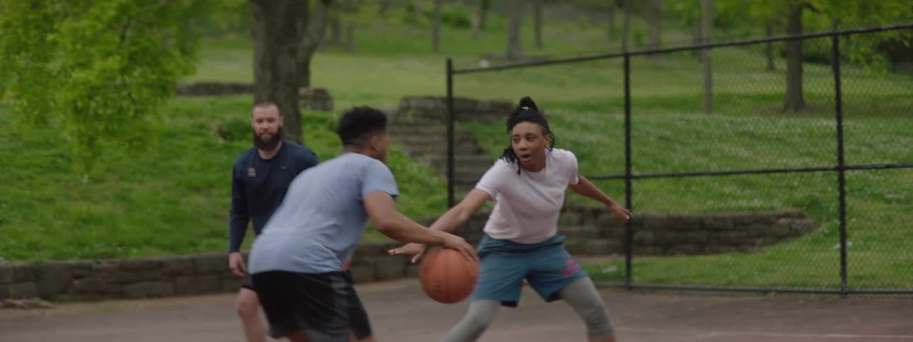 Friends play a casual game of pickup basketball at an outdoor park, ending with a layup in slow motion