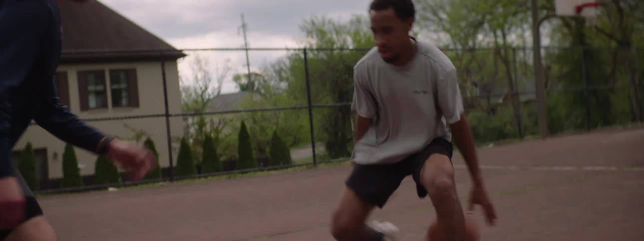 Two men play a friendly but competitive game of one-on-one basketball on an outdoor court in a dynamic slow-motion shot