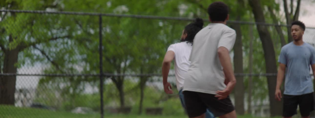 A basketball player skillfully dribbles past a defender and scores a layup in slow motion on an outdoor court