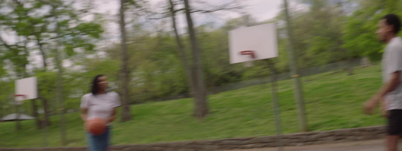 A woman shoots a basketball in slow motion on an outdoor court as the camera follows the ball swishing through the net