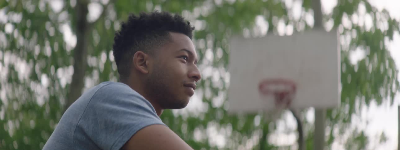 Profile shot of a pensive young man smiling hopefully on an outdoor basketball court