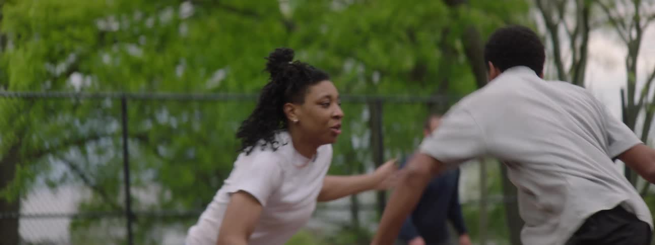 An athletic woman intensely guards a male basketball player dribbling the ball on an outdoor court in slow motion