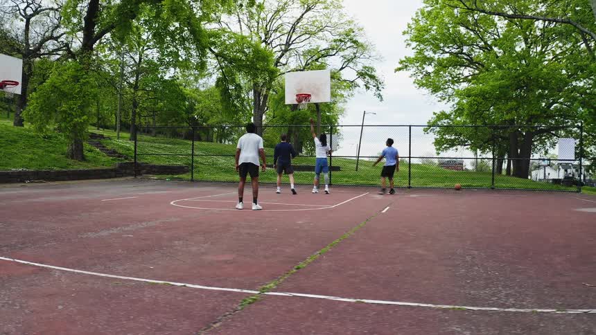 In slow motion, a player scores a layup during a casual basketball game with friends at an outdoor park court