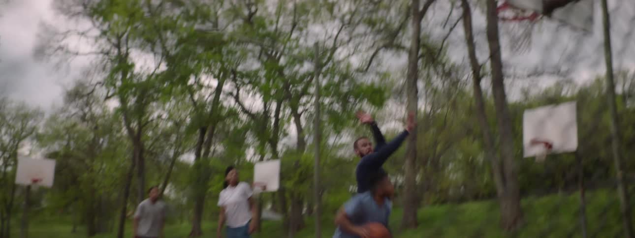 Slow motion shot of a man making a basket while playing streetball with friends at an outdoor court
