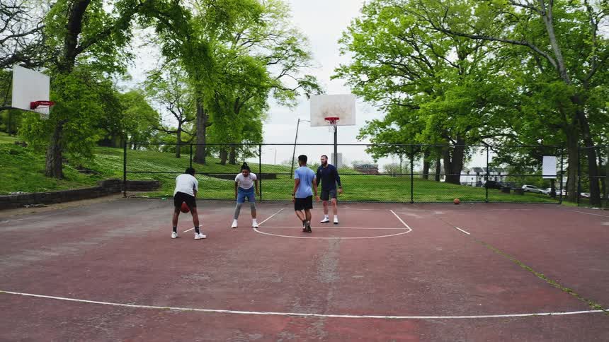 A diverse group of friends play a casual game of basketball at an outdoor park, with one player making a successful jump shot in slow motion