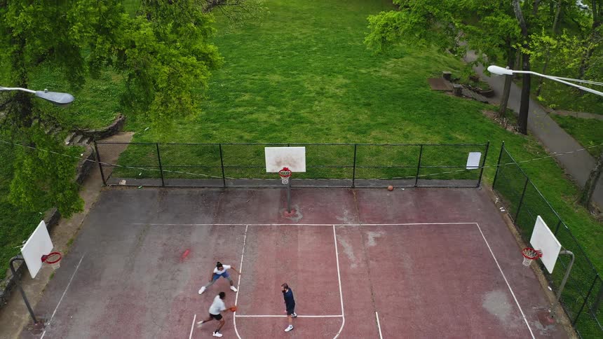 An aerial top-down view pulls up to reveal friends playing basketball on an outdoor court surrounded by a lush green park
