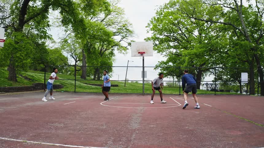 A group of diverse friends plays a spirited game of pickup basketball in slow motion on a court in the park