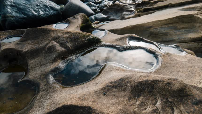 A time-lapse of clouds reflecting in tide pools formed in unique sandstone rock formations on a sunny day