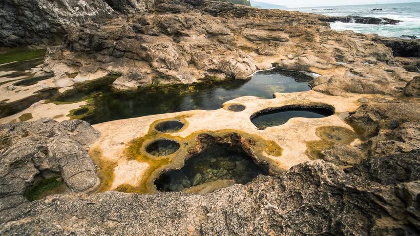 Eroded sandstone rock formations create unique tide pools along the ocean's edge in a tranquil timelapse