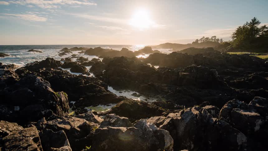 A slow dolly shot reveals a majestic, rocky coastline as the golden sunset reflects off the crashing ocean waves