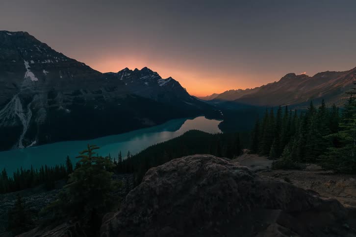 A stunning timelapse captures the sunrise over a majestic mountain range, illuminating a vibrant turquoise lake in the valley below