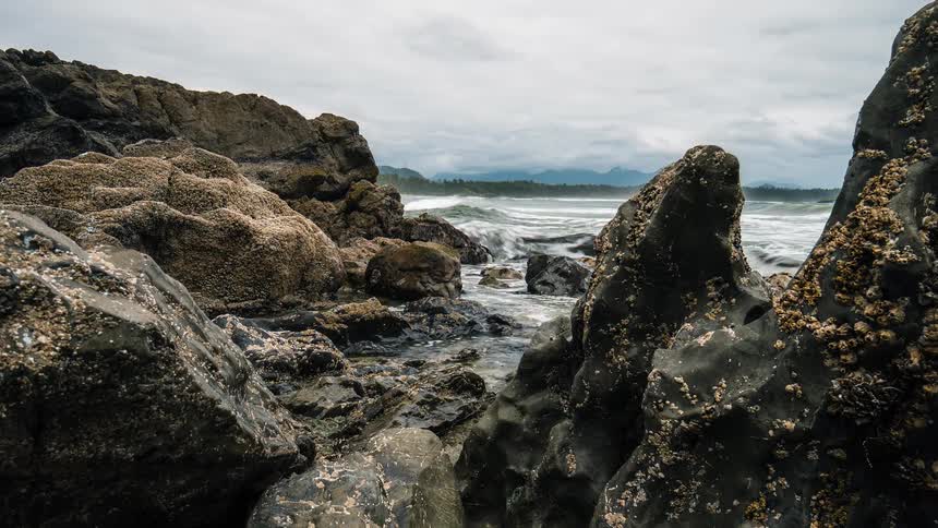 A time-lapse of powerful ocean waves crashing over a rugged, rocky coastline on a moody, overcast day
