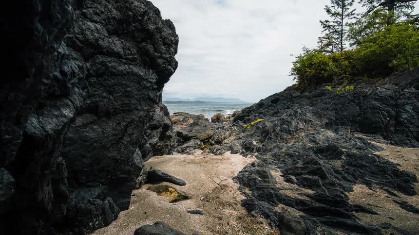 A time-lapse view from a sandy cove framed by dark volcanic rocks shows gentle ocean waves and shifting clouds