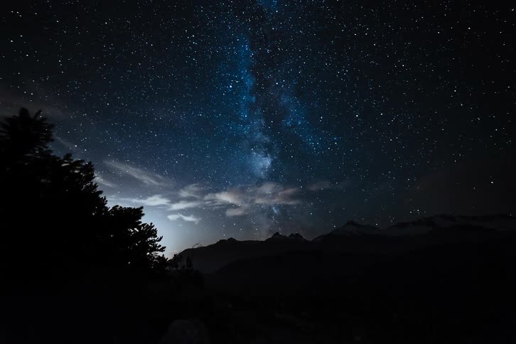 A stunning time-lapse shows the Milky Way and shooting stars moving across the night sky above a silhouetted mountain range as dawn approaches