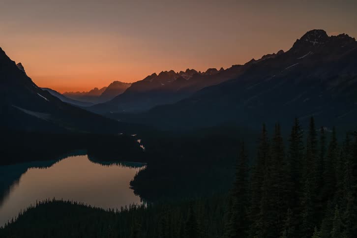 Stunning time-lapse of an orange sunset fading over a vast mountain valley with a serene lake and dense pine forest