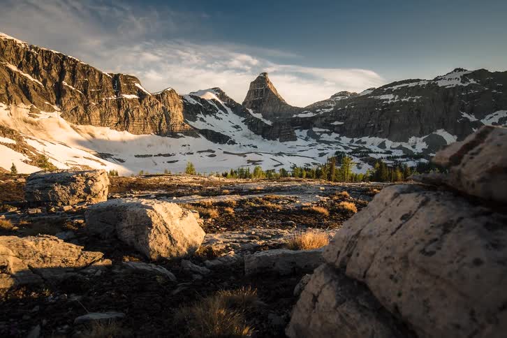 A beautiful golden hour timelapse pans across a rocky alpine landscape as shadows move over the snow-covered mountains