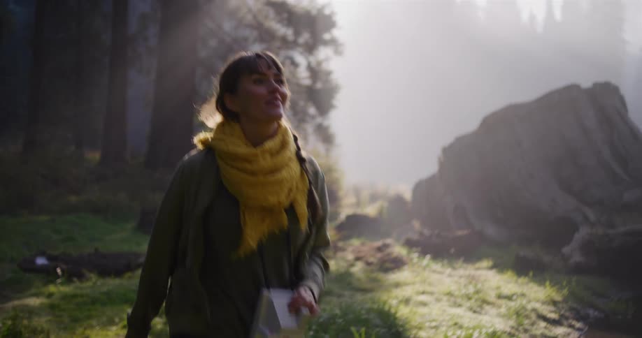 A woman holding a vintage camera happily explores a stunning, foggy redwood forest at sunrise