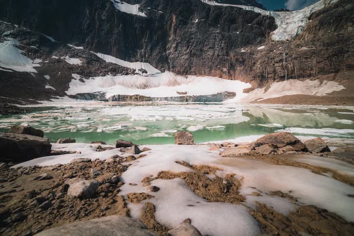 A majestic time-lapse pulls back to reveal a stunning glacial lake with icebergs floating on turquoise water at the base of a rugged mountain range