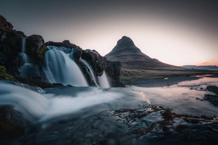 A serene long exposure of Kirkjufellsfoss waterfall flows in front of the iconic Kirkjufell mountain in Iceland during a beautiful sunset