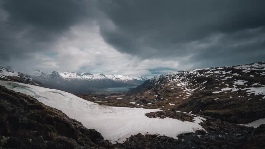 Time-lapse of ominous storm clouds rolling over a vast snowy mountain valley landscape in Norway