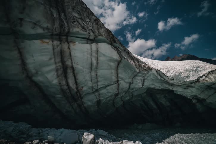 A majestic, slow pull-back shot reveals a massive glacier ice cave in a frozen, mountainous landscape under a bright blue sky