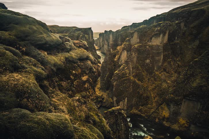A breathtaking view of a river flowing through a majestic and ancient moss-covered canyon in Iceland