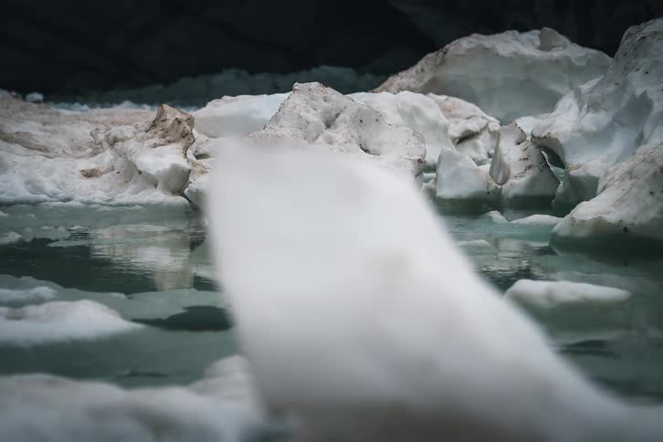 A moody close-up shot of a tranquil pool of glacial meltwater reflecting dirty ice formations inside a dark ice cave