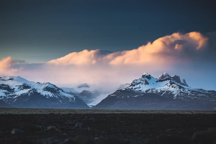 Golden hour timelapse of dramatic clouds rolling over a vast, snow-capped mountain range as day turns to night