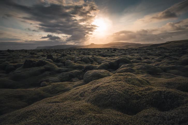 A dramatic timelapse captures sunlight and shadows moving across a vast, moss-covered volcanic landscape as clouds drift overhead