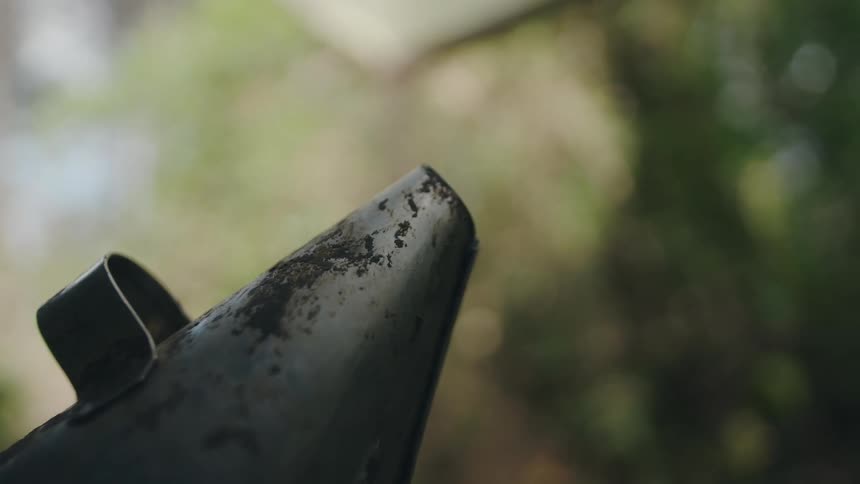 A close-up shot of an old, weathered bee smoker releasing gentle puffs of smoke in an outdoor apiary setting