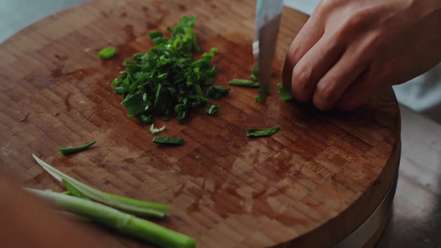 A chef skillfully chops fresh green scallions on a rustic wooden butcher block