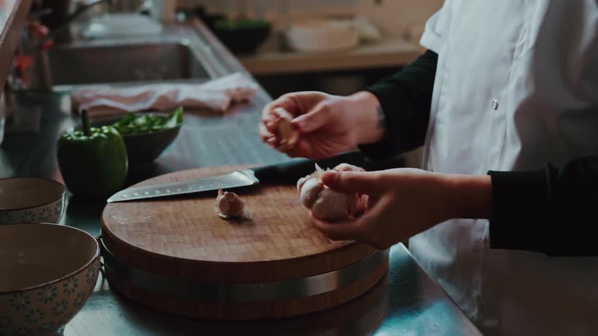 A chef carefully separates garlic cloves from a bulb on a wooden chopping board in a professional kitchen