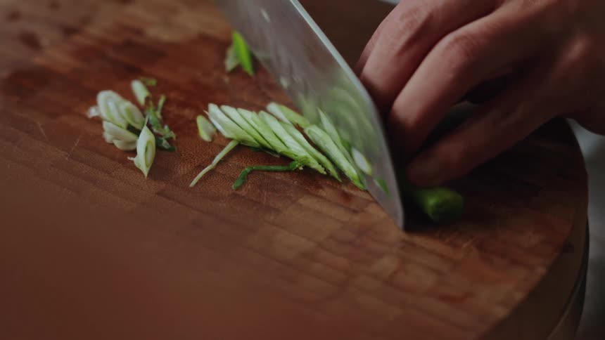 Close-up slow motion shot of a person's hands skillfully chopping fresh green onions on a wooden cutting board