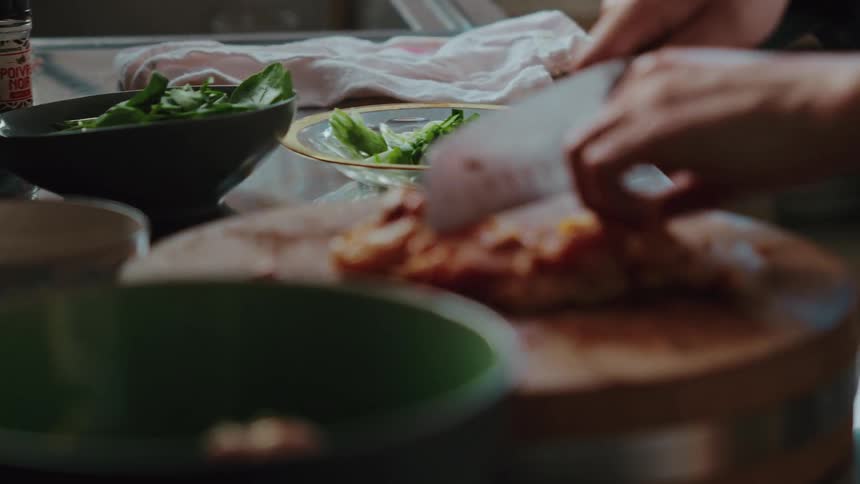 A chef's hands carefully chop marinated meat on a wooden cutting board in a kitchen in slow motion