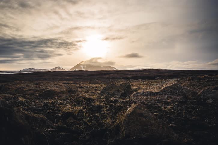 A dramatic time-lapse reveals a vast, rocky landscape as clouds move over a distant snow-capped mountain under a moody sky