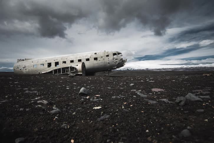 A slow dolly shot moves across the desolate black sand beach, revealing the iconic DC-3 plane wreck at Sólheimasandur, Iceland, under a stormy sky
