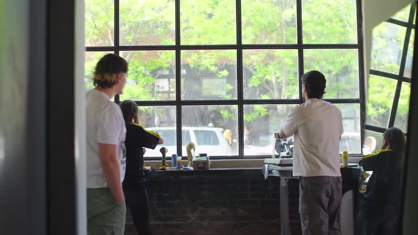 A group of young entrepreneurs use a heat press machine to print t-shirts in their sunlit, industrial-style workshop