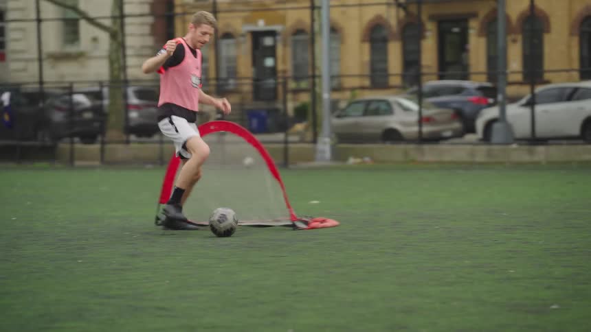 A man skillfully passes a soccer ball to his teammate, who then scores a goal during a slow-motion game on an urban turf field