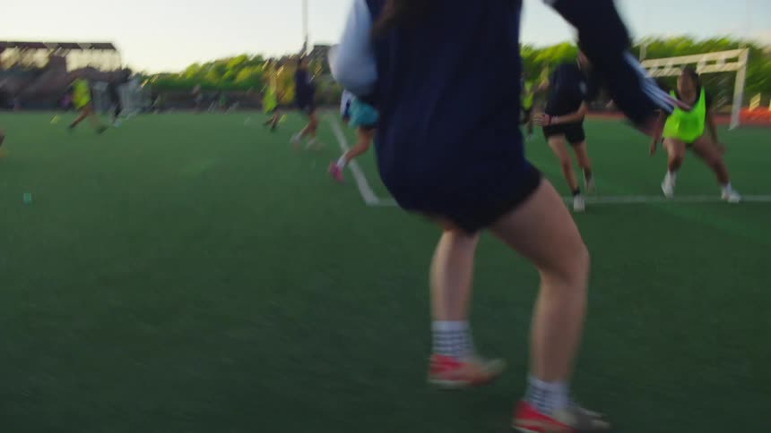 Dynamic slow-motion tracking shot follows female soccer players as they practice dribbling drills on an urban field