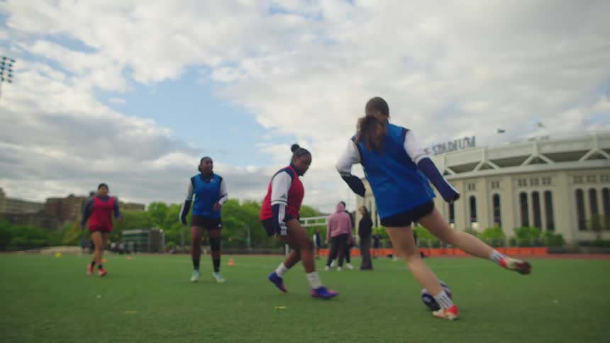 A diverse group of female athletes practice their soccer skills in slow motion on an urban field on a cloudy day