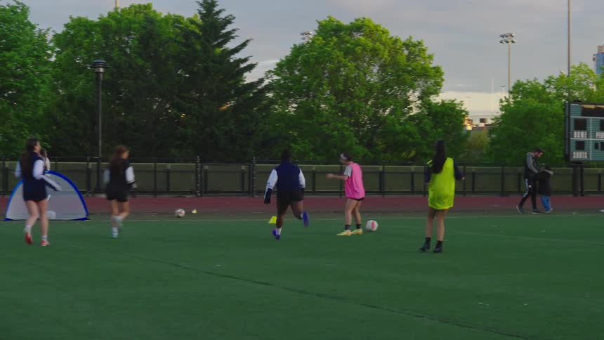 A team of young women passes a soccer ball during practice on a green field in slow motion