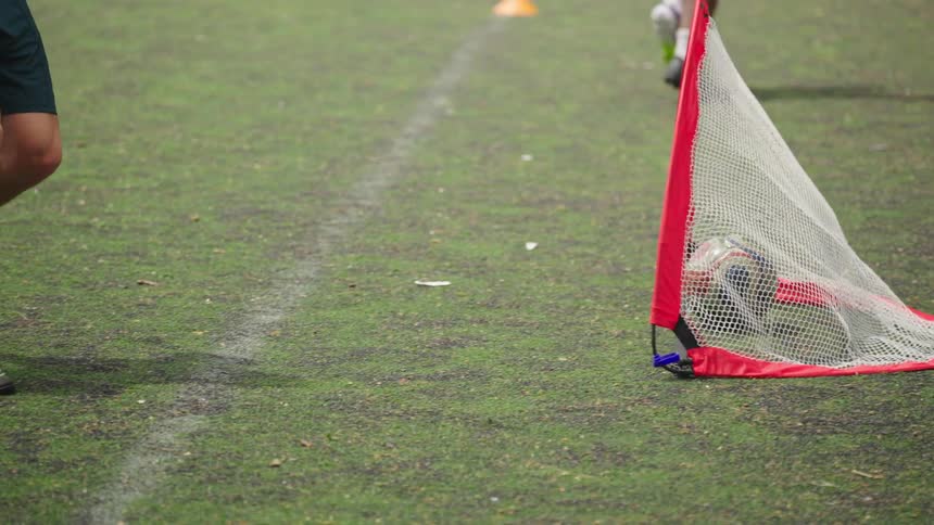 A shirtless soccer player skillfully kicks a ball into the goal during a park game in dramatic slow motion