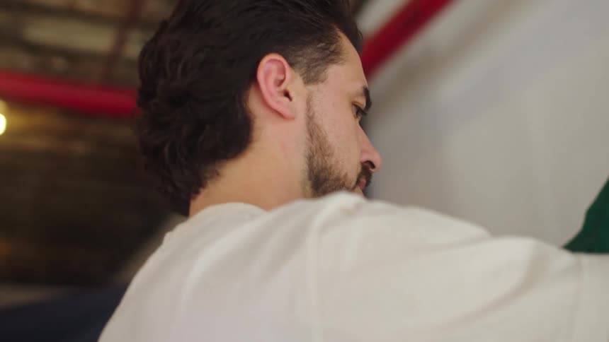 A young man with a mullet and beard carefully browses through a rack of colorful vintage clothes at a secondhand shop